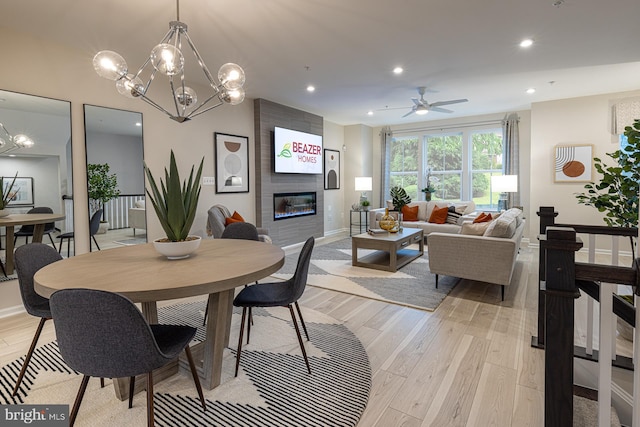 dining area with a fireplace, ceiling fan with notable chandelier, and light hardwood / wood-style flooring