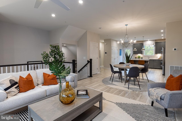 living room with light wood-type flooring and ceiling fan with notable chandelier