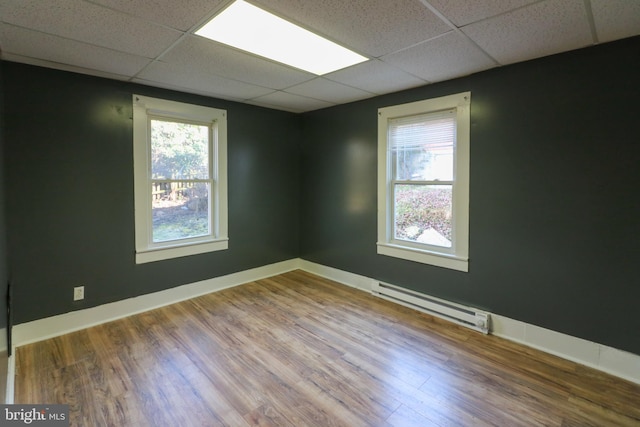 unfurnished room with a drop ceiling, a healthy amount of sunlight, a baseboard heating unit, and dark wood-type flooring