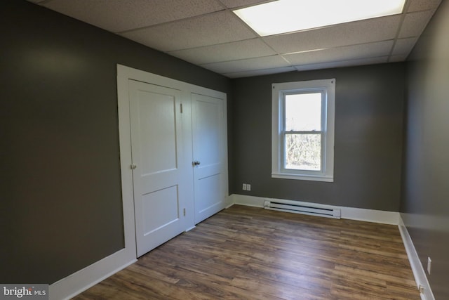 unfurnished bedroom featuring a drop ceiling, dark hardwood / wood-style flooring, and baseboard heating