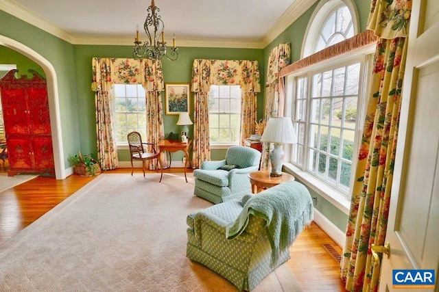 living area with an inviting chandelier, light wood-type flooring, a wealth of natural light, and ornamental molding