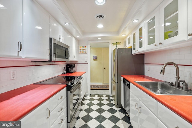 kitchen with backsplash, a tray ceiling, stainless steel appliances, and light tile floors