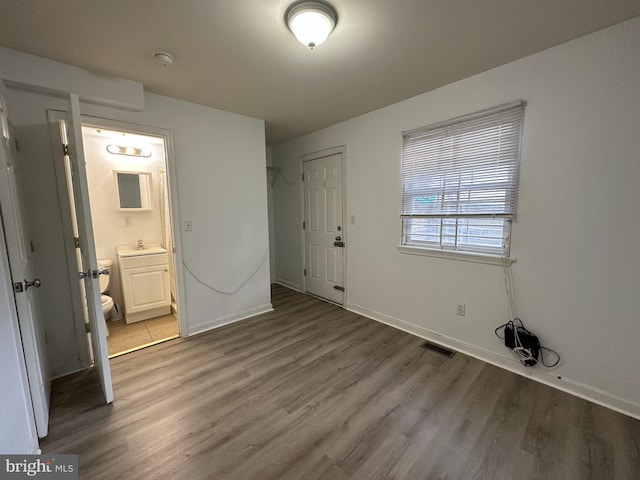 unfurnished bedroom featuring sink, a closet, ensuite bath, and dark wood-type flooring