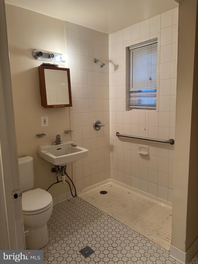 bathroom featuring toilet, sink, tiled shower, and tile flooring