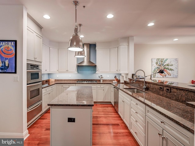 kitchen featuring sink, light hardwood / wood-style flooring, dark stone counters, wall chimney range hood, and pendant lighting