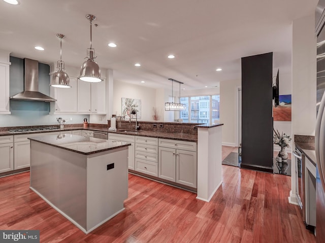kitchen featuring hardwood / wood-style floors, a center island, wall chimney exhaust hood, and pendant lighting