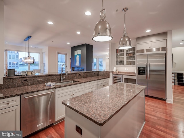 kitchen featuring decorative light fixtures, appliances with stainless steel finishes, white cabinetry, wood-type flooring, and sink