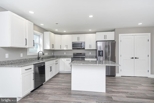 kitchen with appliances with stainless steel finishes, a center island, wood-type flooring, sink, and white cabinets