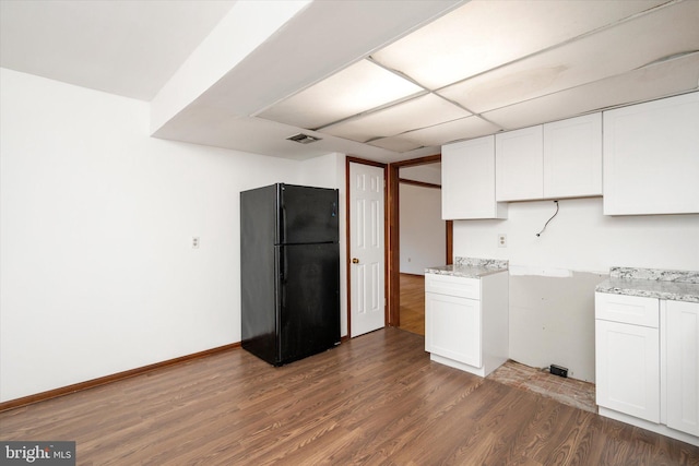 kitchen with white cabinets, hardwood / wood-style flooring, light stone countertops, and black refrigerator