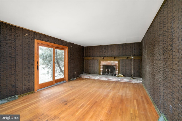 unfurnished living room featuring a fireplace, light hardwood / wood-style floors, and brick wall