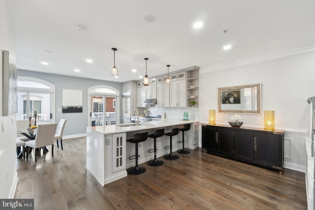 kitchen featuring sink, dark wood-type flooring, hanging light fixtures, a kitchen bar, and kitchen peninsula