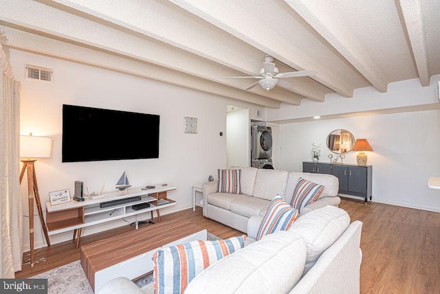 living room featuring dark hardwood / wood-style floors, stacked washer / dryer, ceiling fan, and beamed ceiling