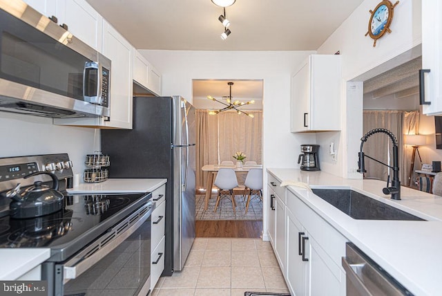 kitchen featuring sink, appliances with stainless steel finishes, light tile flooring, an inviting chandelier, and white cabinetry