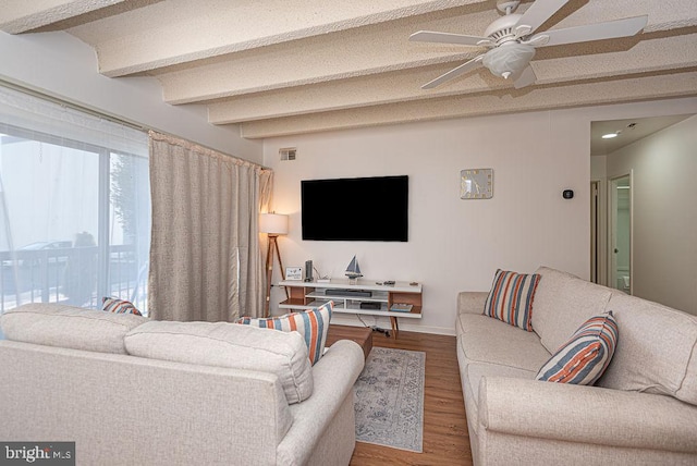 living room featuring ceiling fan, a textured ceiling, beamed ceiling, and wood-type flooring