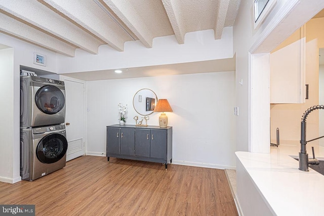 laundry room featuring light wood-type flooring, a textured ceiling, and stacked washer and clothes dryer