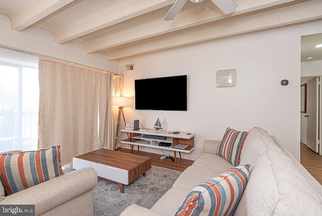 living room with light wood-type flooring, ceiling fan, a textured ceiling, and beamed ceiling