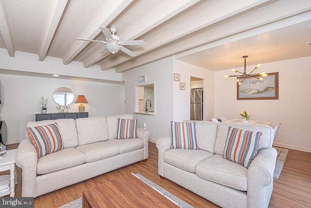 living room with ceiling fan with notable chandelier, beamed ceiling, sink, light wood-type flooring, and a textured ceiling