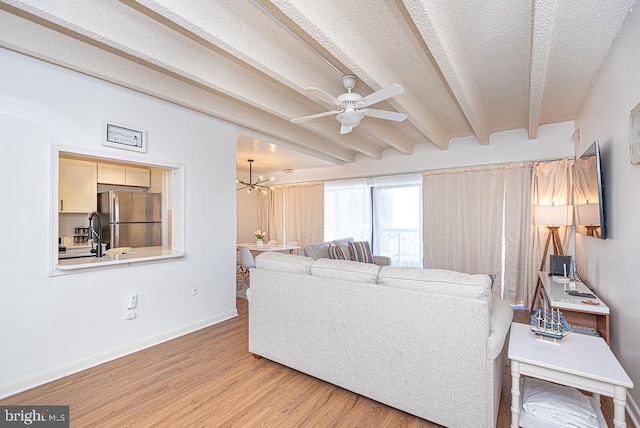 living room with light hardwood / wood-style floors, ceiling fan with notable chandelier, a textured ceiling, and beamed ceiling