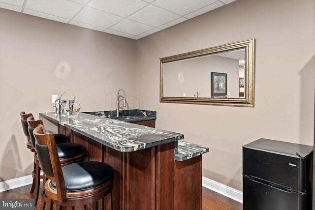 bar with a paneled ceiling, dark stone counters, sink, and dark hardwood / wood-style flooring