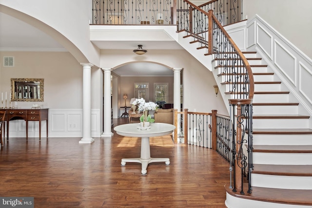 foyer with a towering ceiling, crown molding, dark hardwood / wood-style flooring, and ornate columns