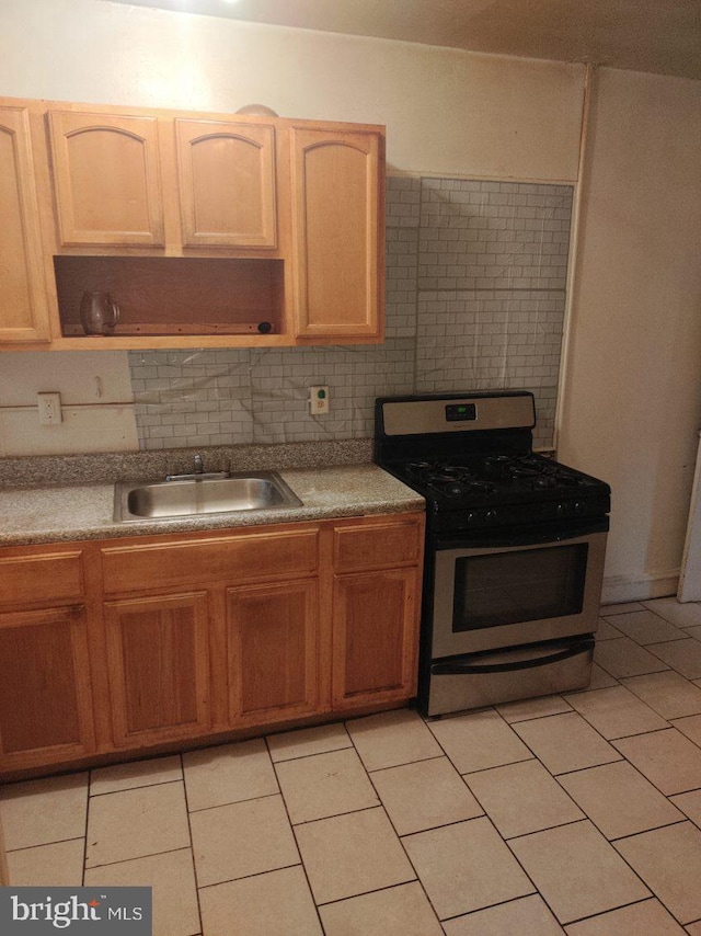 kitchen with tasteful backsplash, light brown cabinetry, light tile floors, gas range, and sink