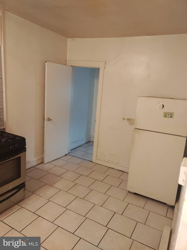 kitchen with light tile flooring, stainless steel range with gas cooktop, white cabinets, and white fridge