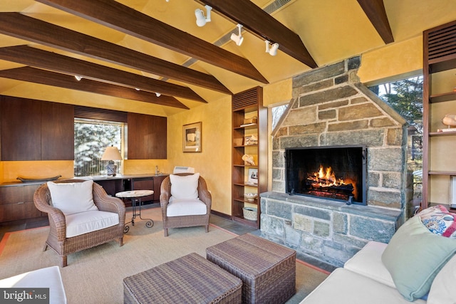 living room featuring a stone fireplace, beam ceiling, rail lighting, and a wealth of natural light