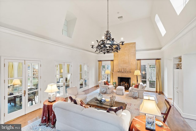 living room featuring light hardwood / wood-style floors, high vaulted ceiling, a skylight, a large fireplace, and an inviting chandelier