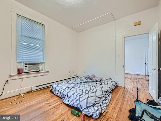 bedroom featuring cooling unit, light wood-type flooring, and a baseboard heating unit