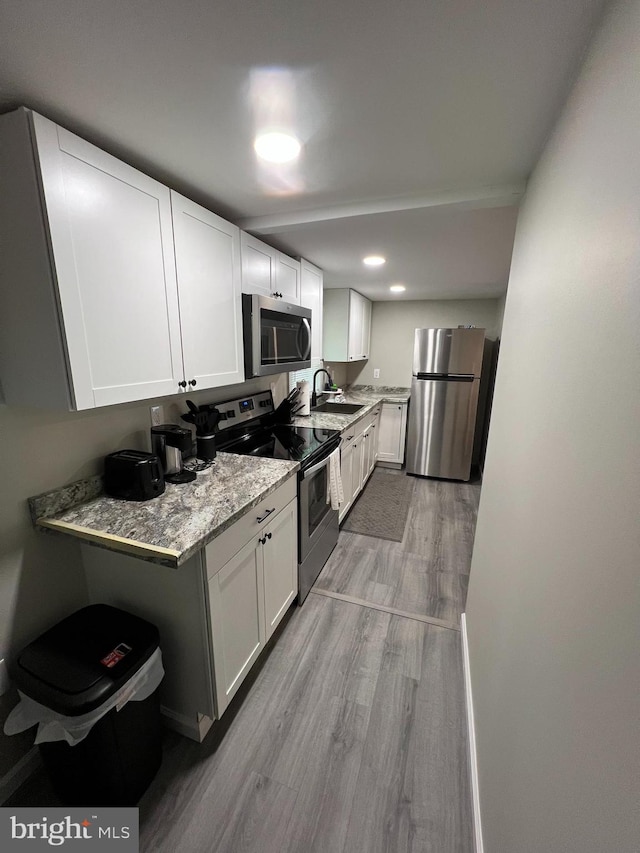 kitchen featuring white cabinets, appliances with stainless steel finishes, light stone countertops, and light wood-type flooring