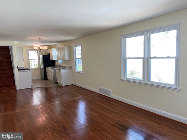 spare room featuring an inviting chandelier, plenty of natural light, and dark hardwood / wood-style flooring