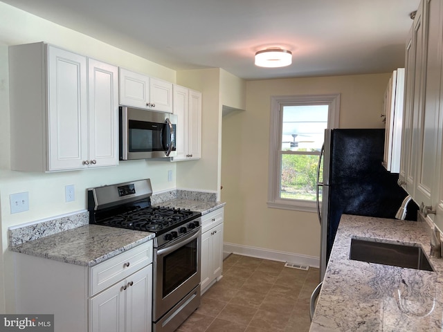 kitchen with white cabinetry, appliances with stainless steel finishes, sink, light stone counters, and dark tile flooring