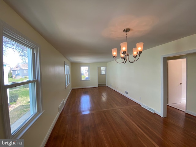 unfurnished room with plenty of natural light, dark hardwood / wood-style floors, and a chandelier