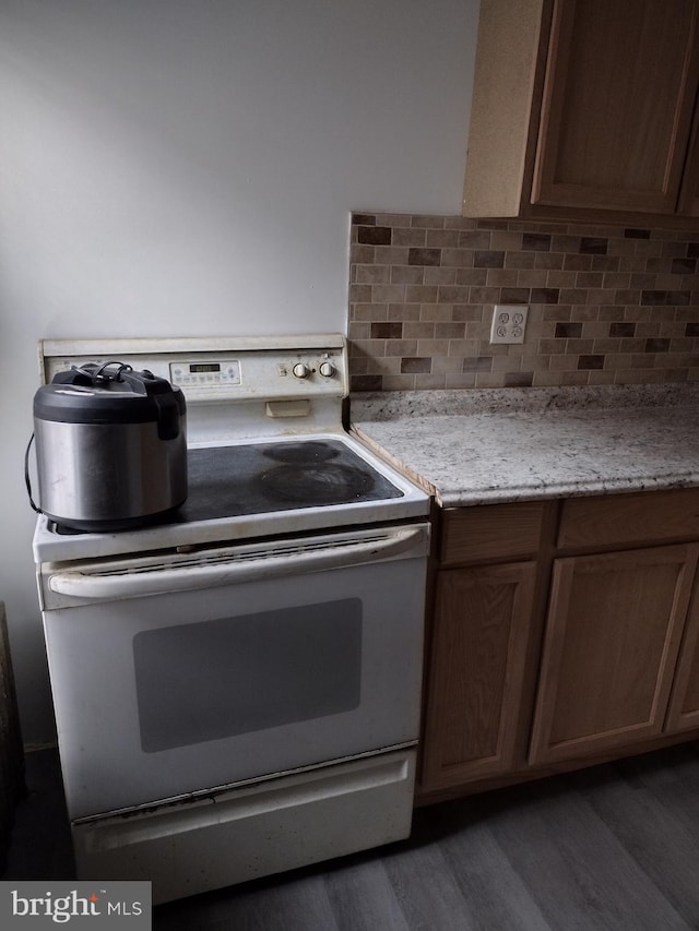 kitchen with dark hardwood / wood-style flooring, electric range oven, tasteful backsplash, and light stone countertops