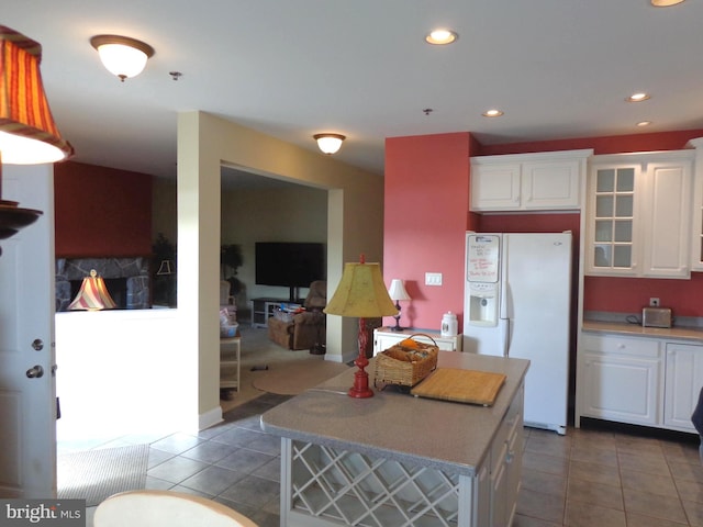 kitchen with a kitchen island, white fridge with ice dispenser, light tile floors, and white cabinets