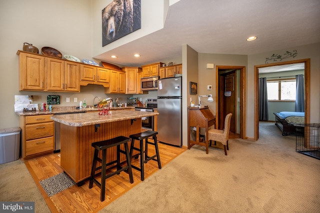 kitchen with appliances with stainless steel finishes, light carpet, a kitchen bar, an island with sink, and light stone countertops