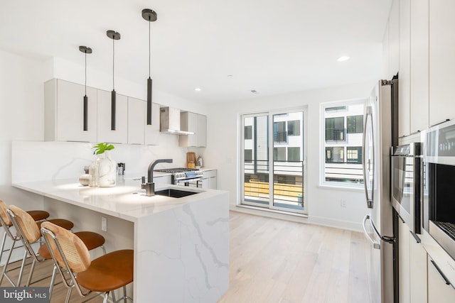 kitchen with a kitchen breakfast bar, light wood-type flooring, light stone countertops, and wall chimney exhaust hood