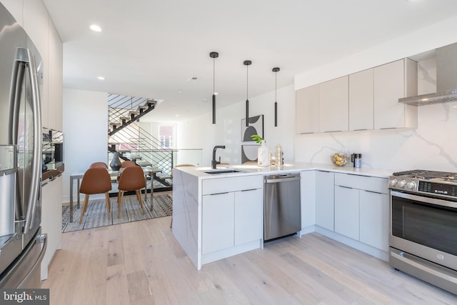 kitchen featuring pendant lighting, stainless steel appliances, kitchen peninsula, light hardwood / wood-style flooring, and backsplash