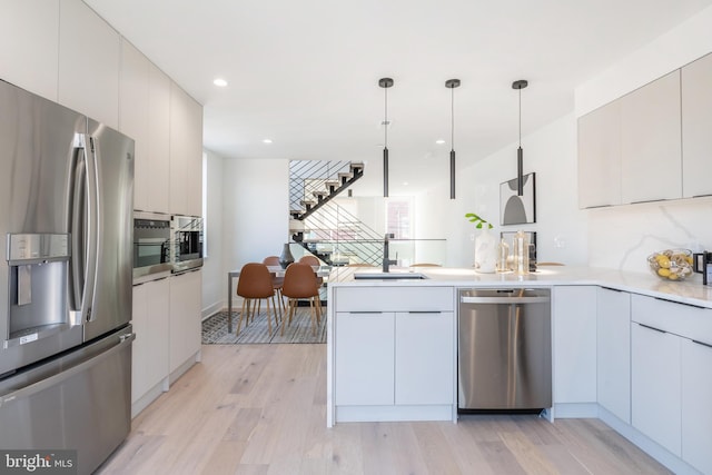 kitchen with decorative light fixtures, white cabinetry, light hardwood / wood-style floors, sink, and stainless steel appliances