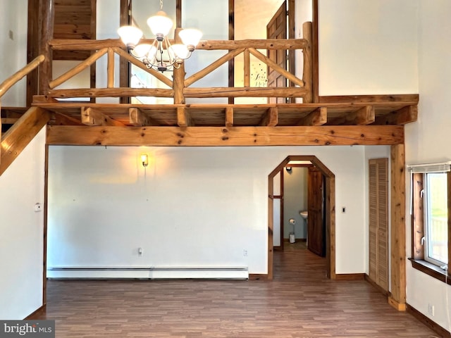 empty room with dark hardwood / wood-style floors, a notable chandelier, and a baseboard heating unit