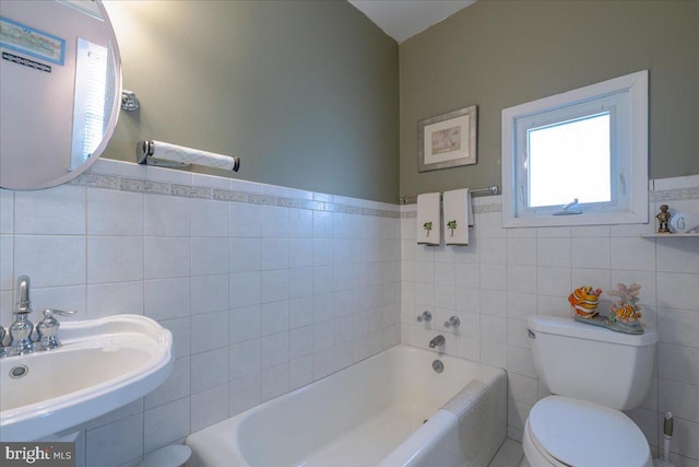 bathroom with a washtub, toilet, sink, and tile walls