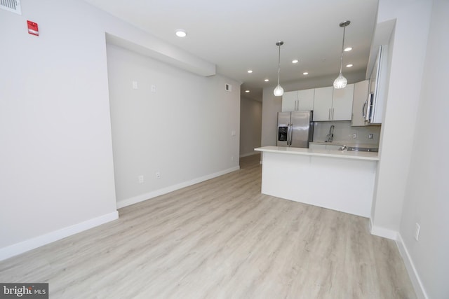 kitchen with light hardwood / wood-style floors, stainless steel appliances, decorative light fixtures, white cabinetry, and backsplash