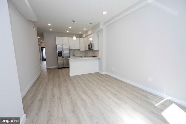 kitchen featuring light hardwood / wood-style floors, decorative light fixtures, kitchen peninsula, appliances with stainless steel finishes, and white cabinets