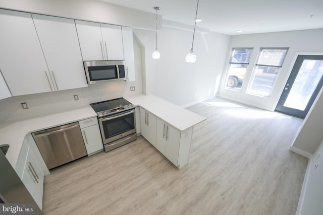 kitchen with decorative light fixtures, appliances with stainless steel finishes, white cabinetry, kitchen peninsula, and light wood-type flooring