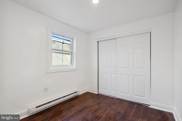 unfurnished bedroom with a closet, a baseboard radiator, and dark wood-type flooring