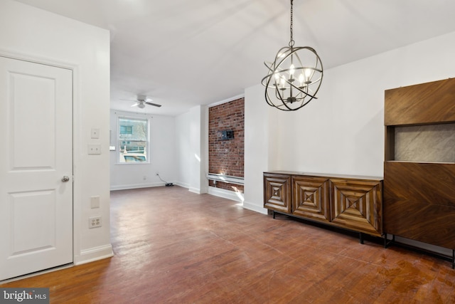 interior space with brick wall, dark wood-type flooring, and ceiling fan with notable chandelier