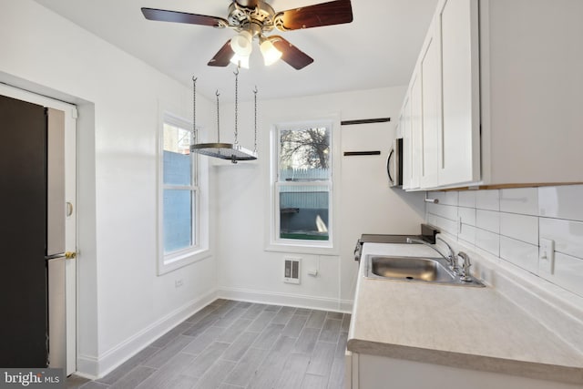 kitchen with tasteful backsplash, white cabinetry, wood-type flooring, ceiling fan, and sink