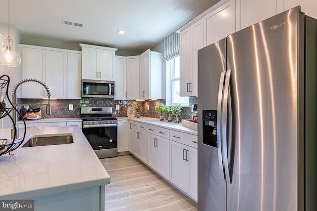 kitchen with pendant lighting, light stone countertops, tasteful backsplash, appliances with stainless steel finishes, and white cabinetry