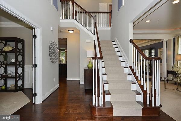 stairs with crown molding, dark hardwood / wood-style floors, decorative columns, and a high ceiling