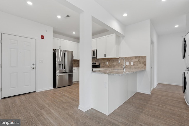 16423 River View Dr, Bristol, PA 19007 - kitchen with appliances with stainless steel finishes, stacked washing machine and dryer, light stone countertops, tasteful backsplash, and light wood-style floors